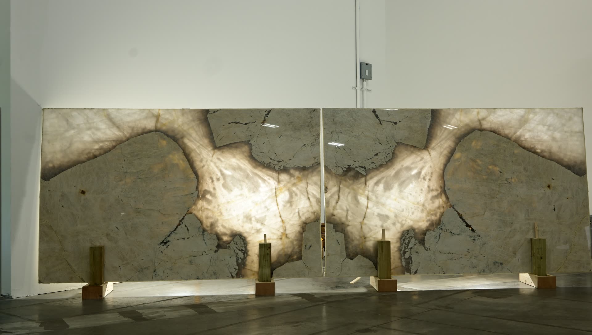 A mirrored pair of stone panels standing side by side, lit from behind so the pattern glows through, with the two halves forming a symmetrical figure across the join.