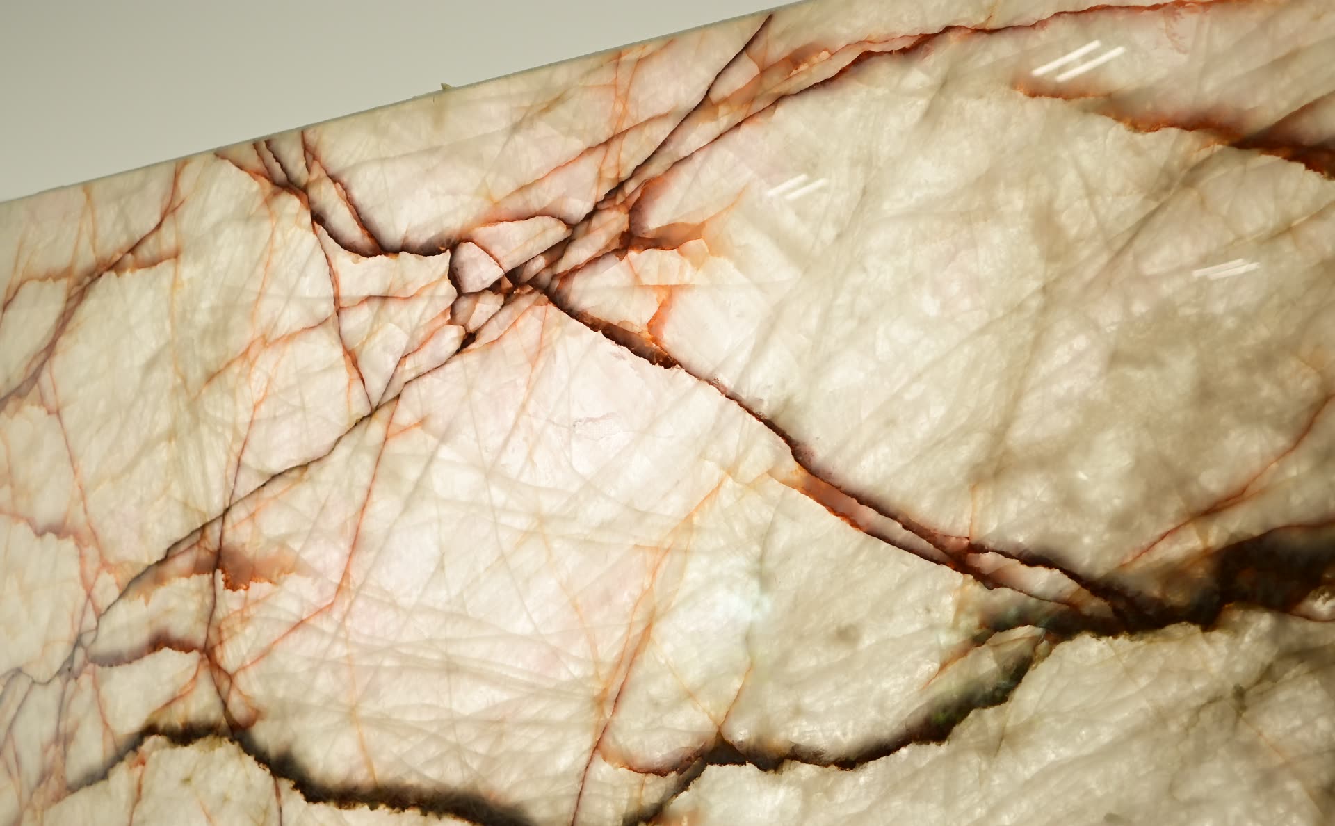 Close view of a translucent pale stone surface with fine orange and brown veins running across it.