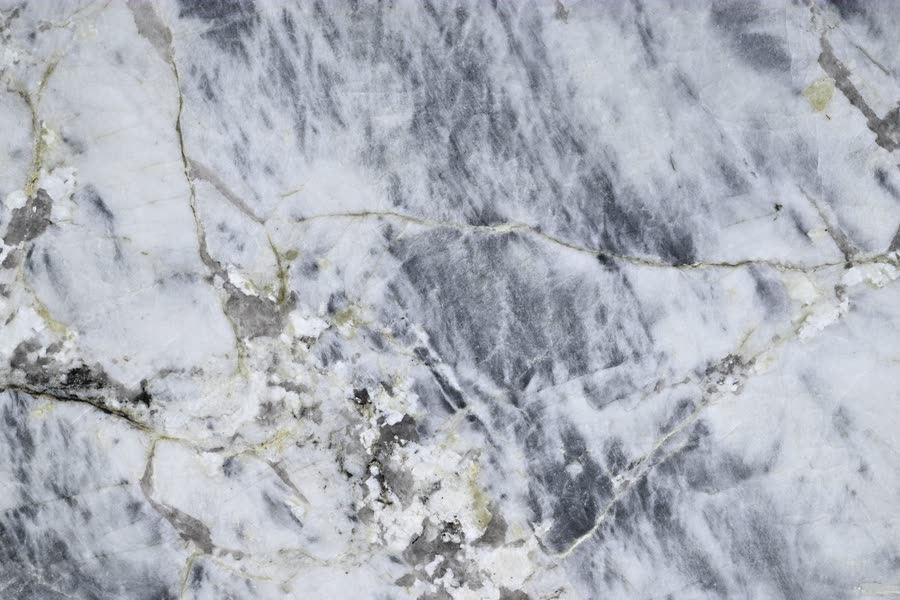 Close view of a polished Blue Alpine surface: a grey-blue and white veined ground broken by pale translucent patches and a branching network of thin olive-gold veins.
