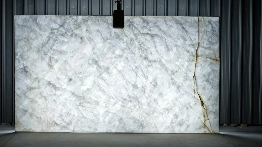 A large Crystallo Traslux slab standing upright against corrugated metal siding, held by an overhead lifting clamp, photographed on a concrete floor.