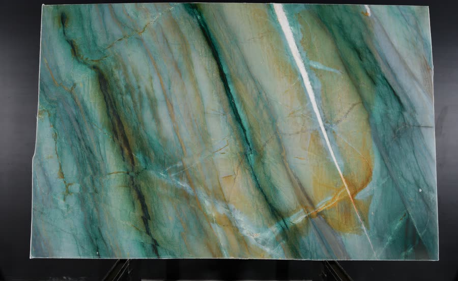A full Mocamblu slab upright on a display rack, flowing with aqua, teal and gold veining and a bright white vein running from top to bottom.