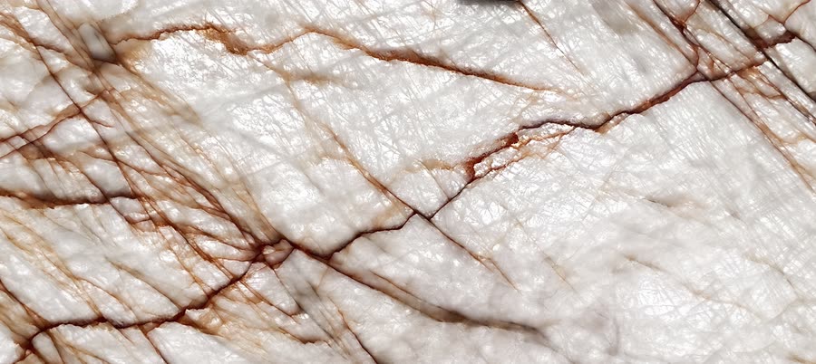 Rosso Crystallo lit from behind: a warm white translucent surface threaded with fine dark brown and rust veins that branch across the frame like bare tree limbs.
