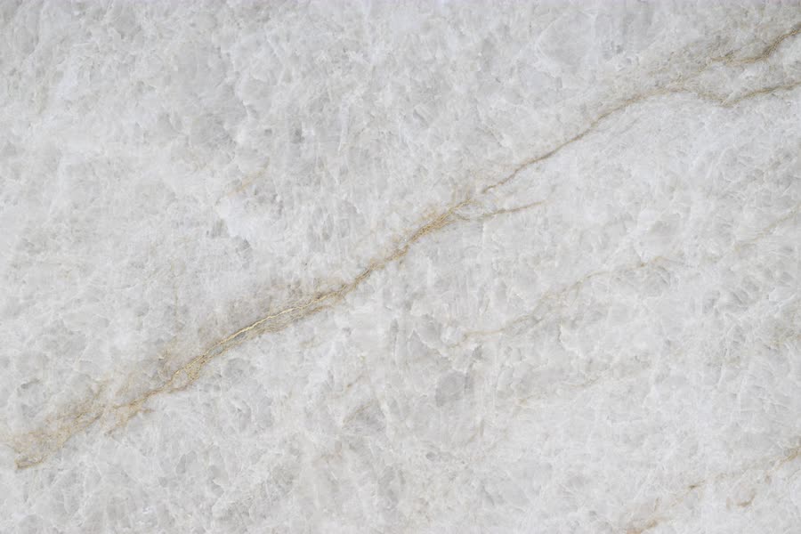 Extreme close-up of a translucent white crystalline stone surface, its icy facets shot through with a thin golden-brown vein running diagonally from lower left to upper right.