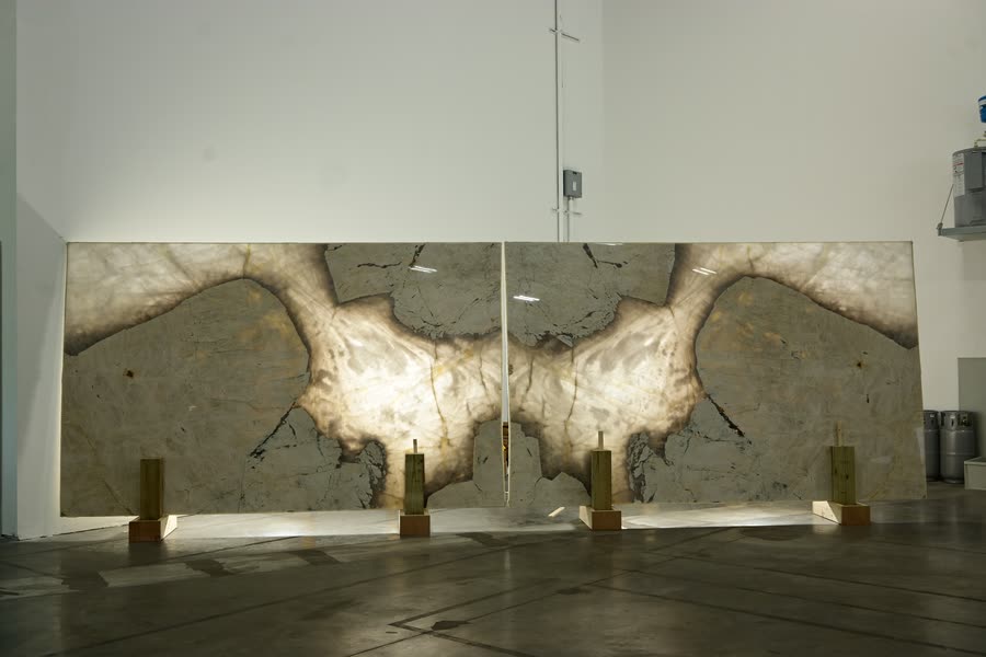 A bookmatched pair of stone slabs standing side by side on metal stands, mirrored so their pale, cloud-like veining forms one symmetrical pattern across both panels.