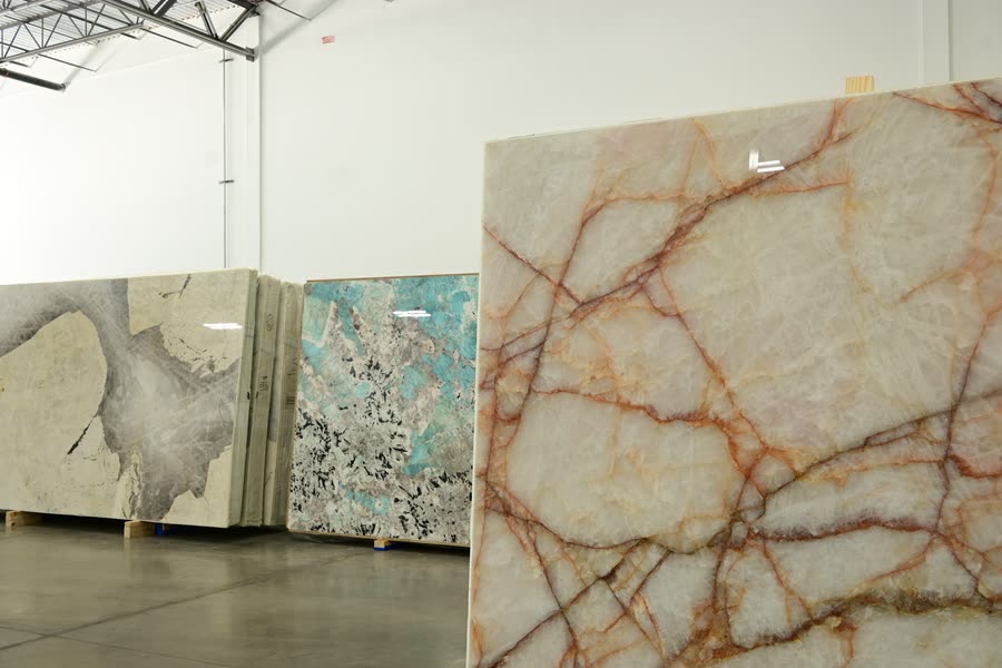 A translucent pale slab with branching orange-red veins standing upright at the front of a row of slabs, with further slabs displayed on pallets behind it.