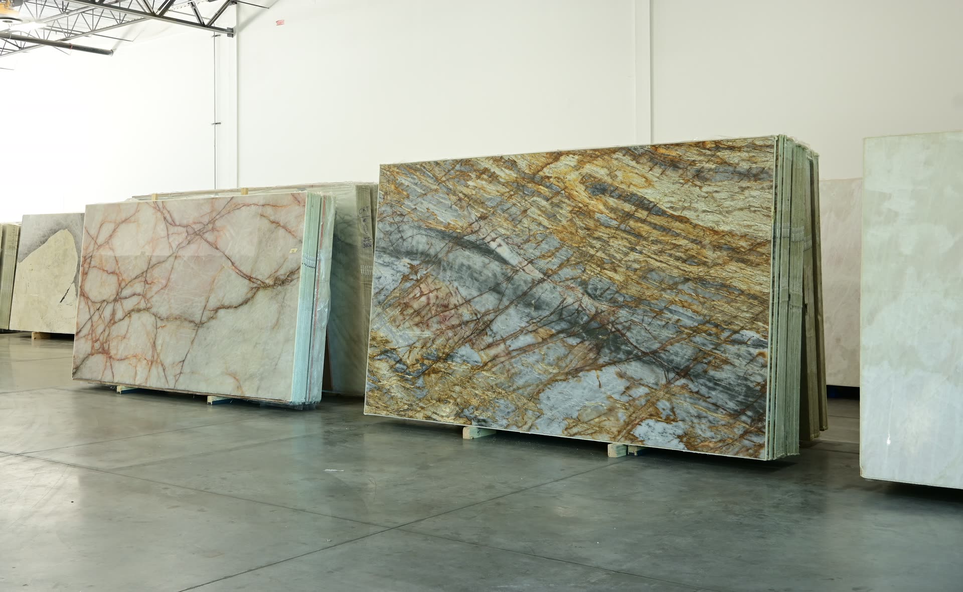 Full stone slabs at the West Palm Beach showroom, with a gold and blue-grey veined slab at the centre and a pale rose-veined slab beside it.